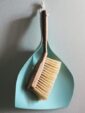 A wooden-handled brush and blue dustpan hanging on a wall, offering a minimalist look.